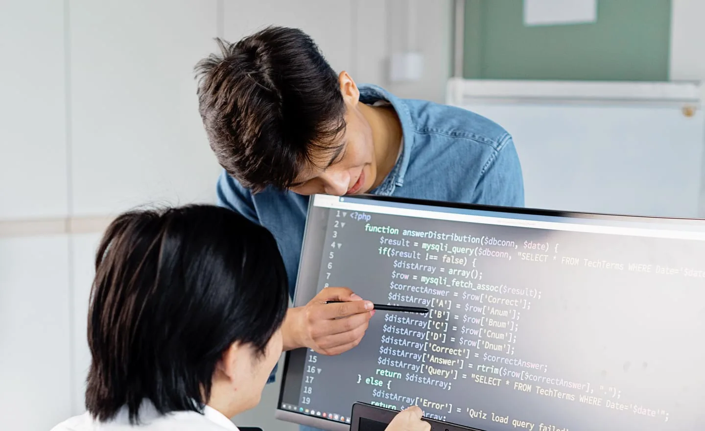 Two engineers talk through a block of code on a monitor.