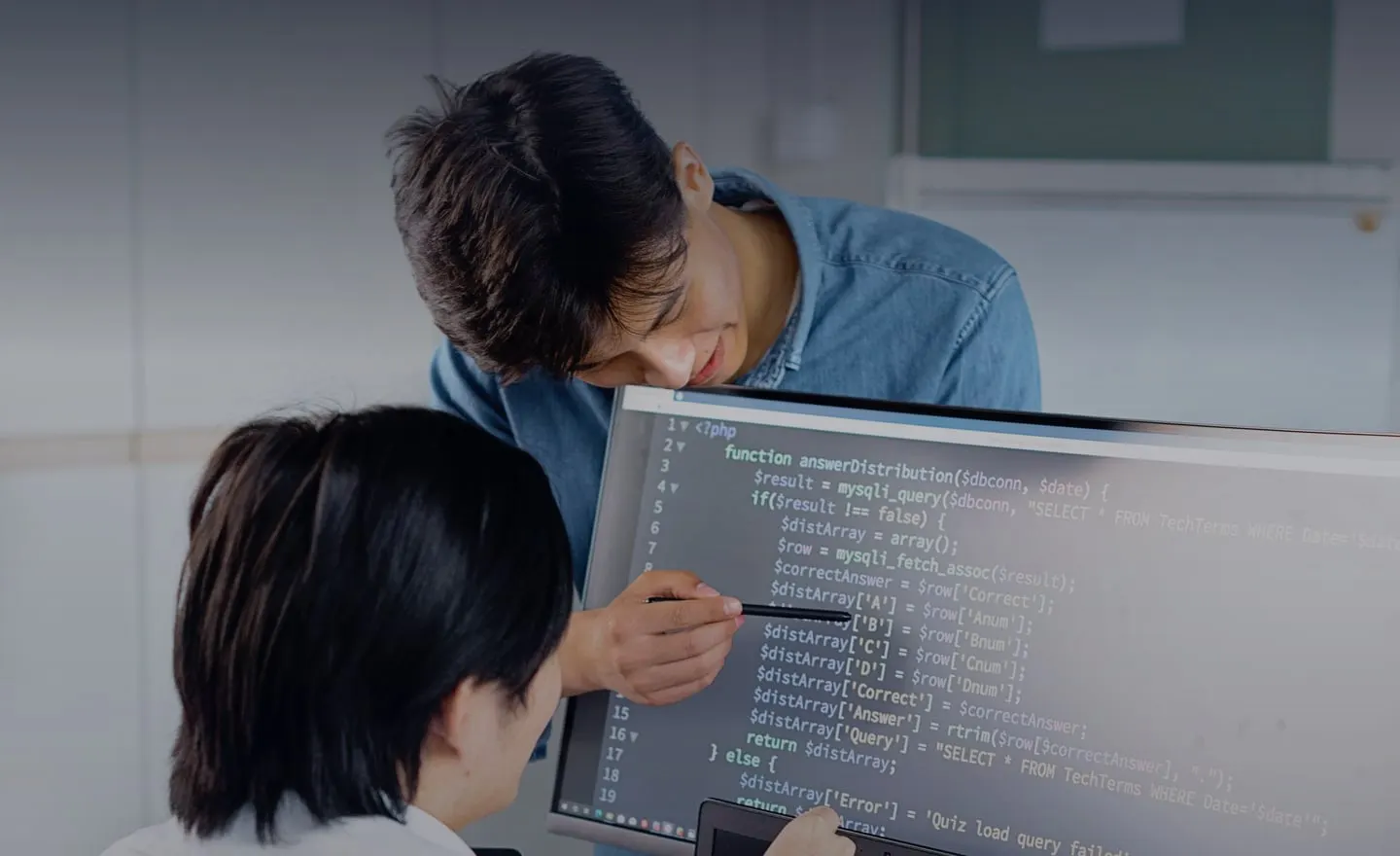 Two engineers review code together on a monitor.