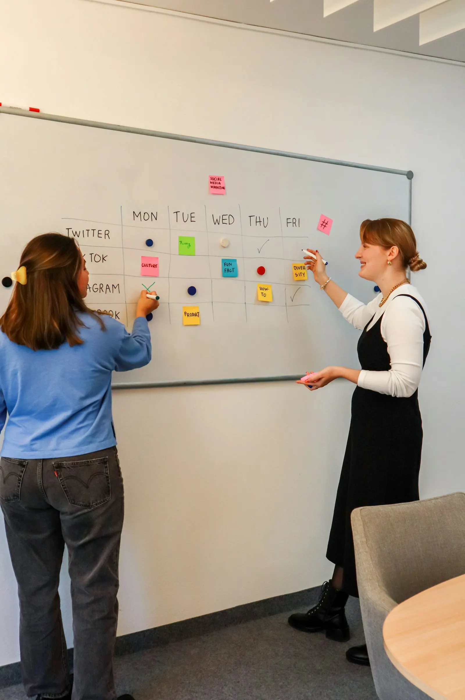 Two product managers plan a roadmap on a whiteboard of sticky notes.