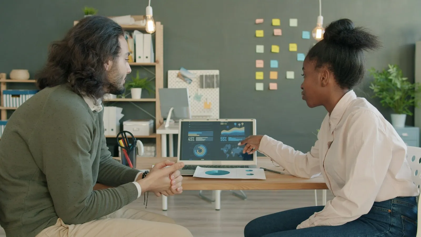 Product managers review a delivery dashboard on a laptop at a shared desk.