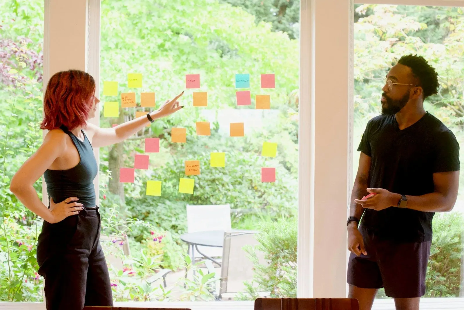 Two colleagues sort sticky notes on a window during a planning session.
