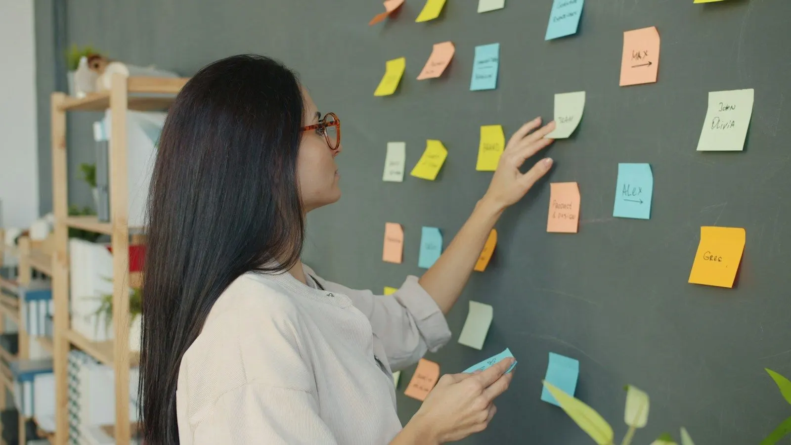 A woman in glasses places sticky notes on a dark planning wall.
