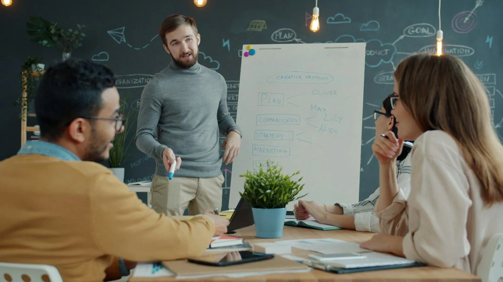 A team lead walks colleagues through a delivery plan at a whiteboard.