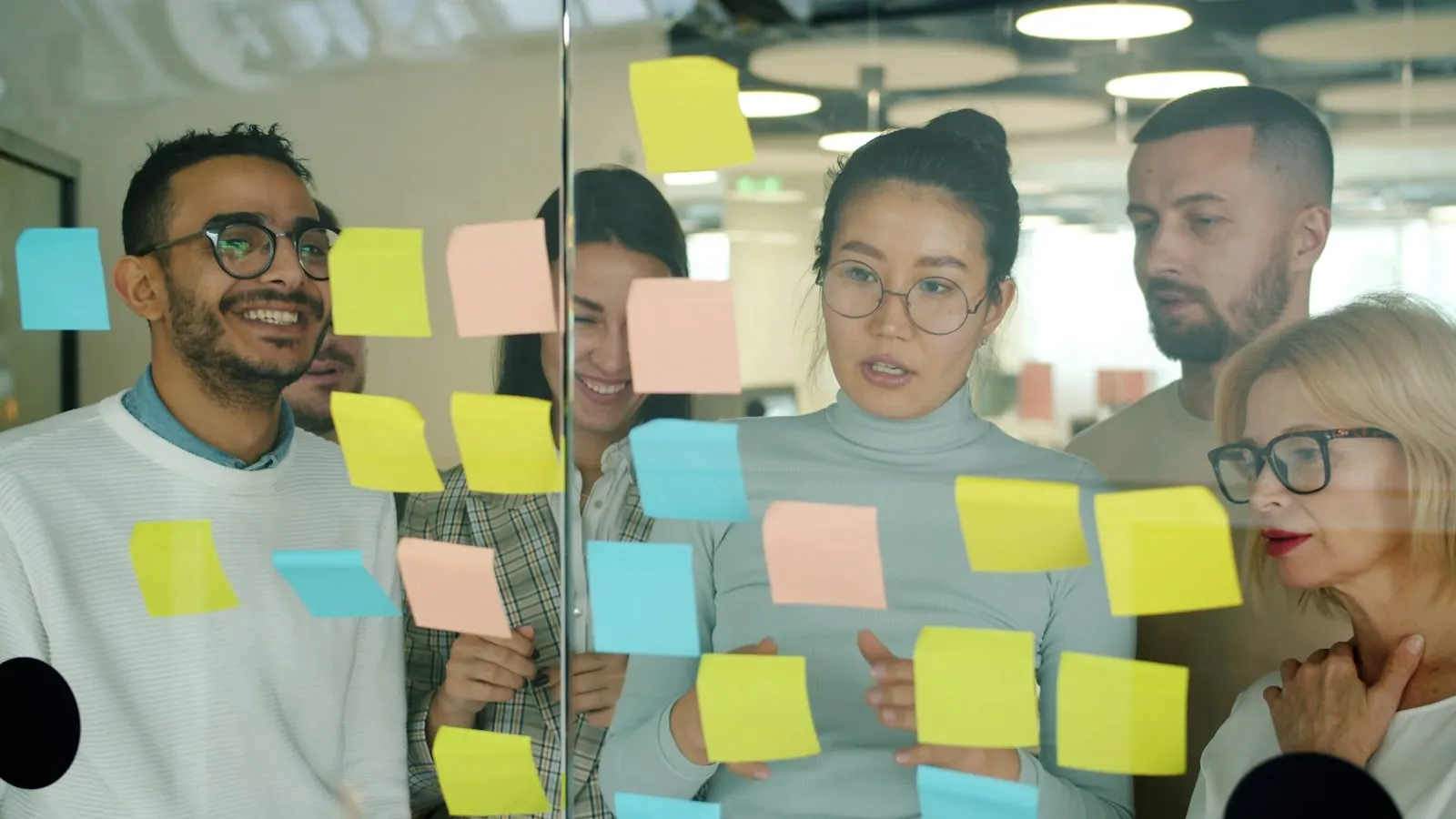 A UI/UX design team sorting sticky notes on a glass wall during a research session.