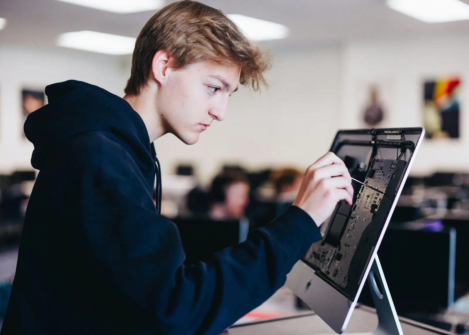 A UX researcher in a hoodie works with a stylus on a touchscreen computer in an office.