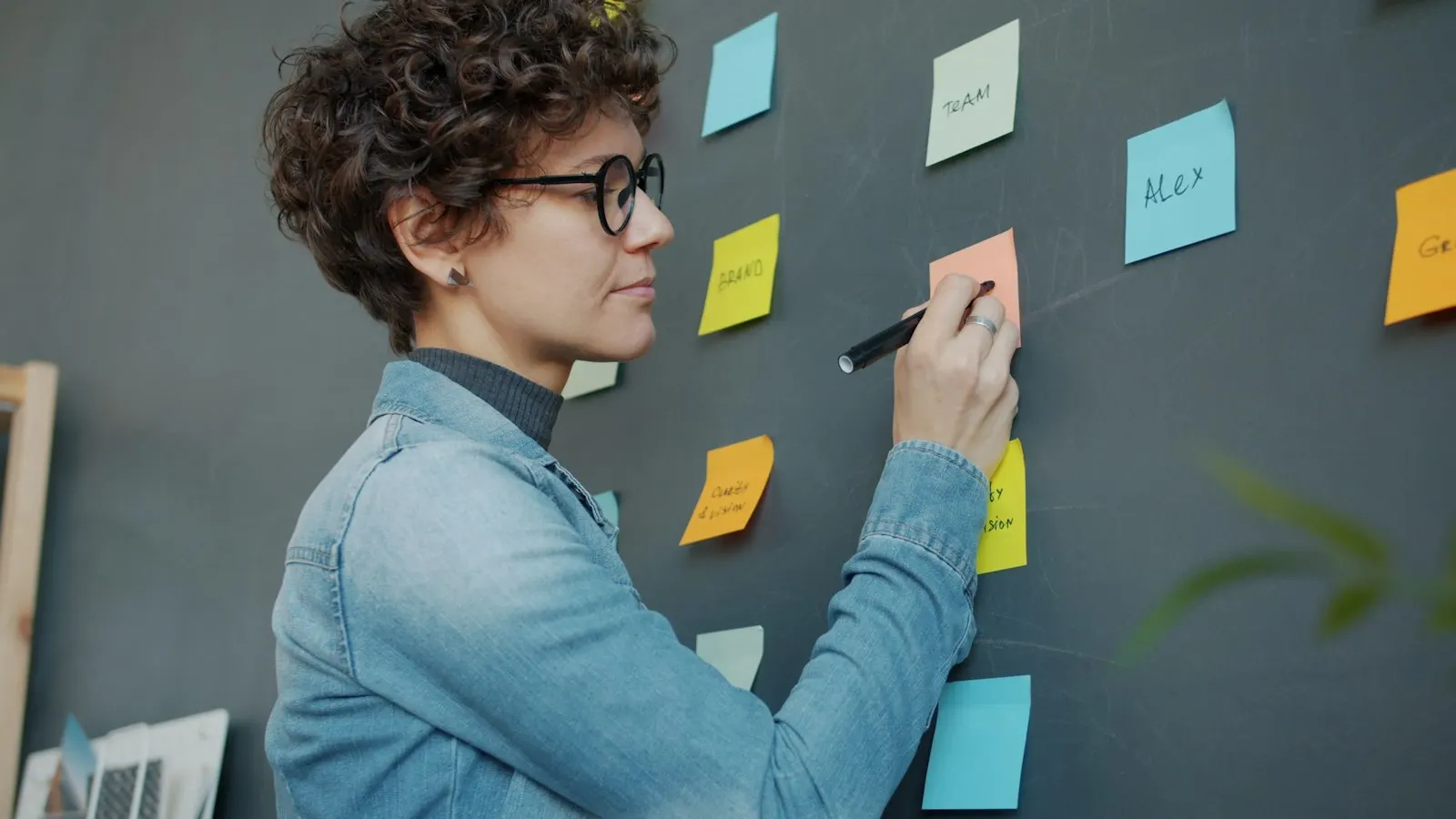A business analyst writing on sticky notes on a dark wall during a requirements workshop.