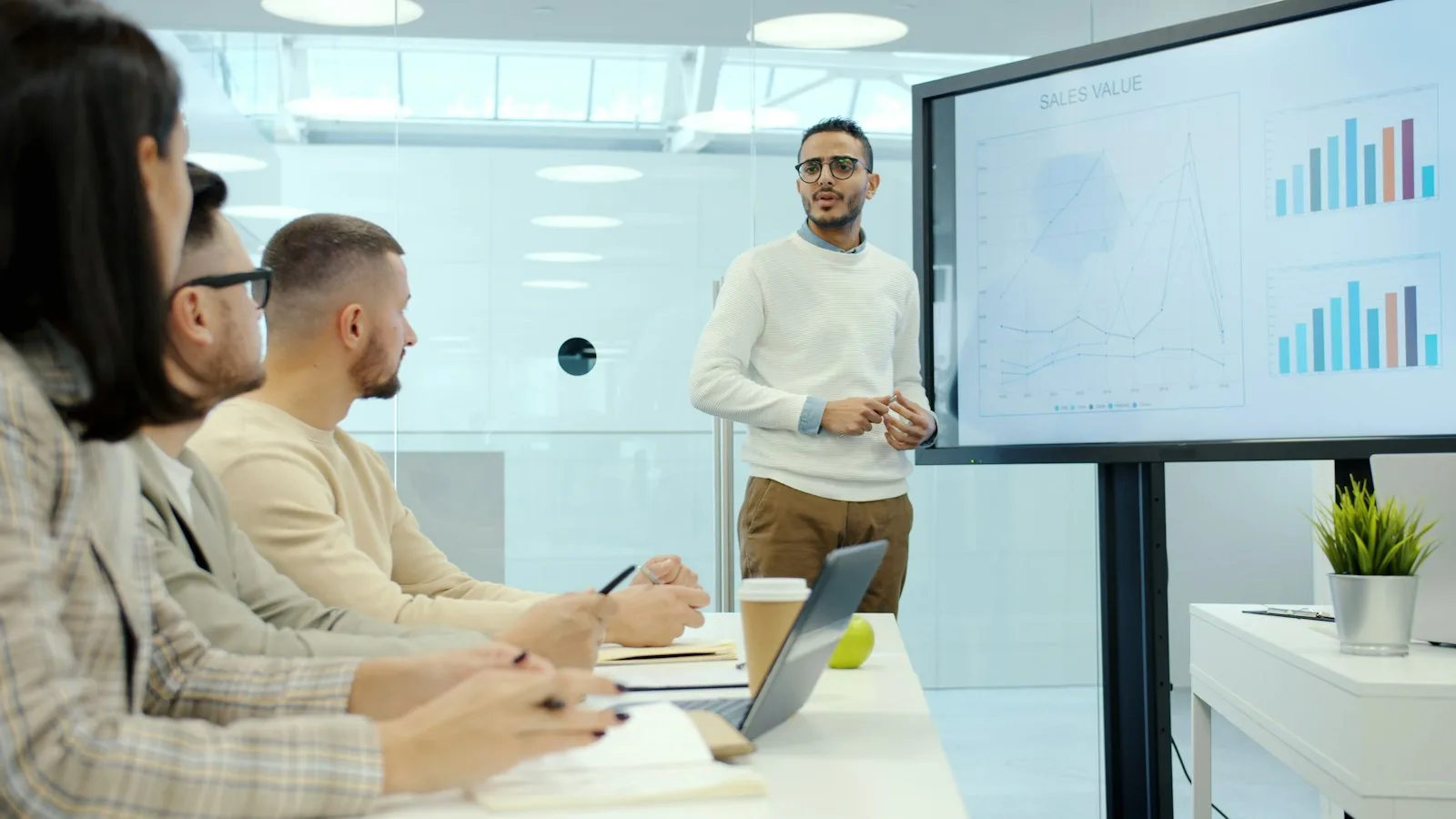 A business analyst presenting charts on a screen to colleagues around a meeting table.