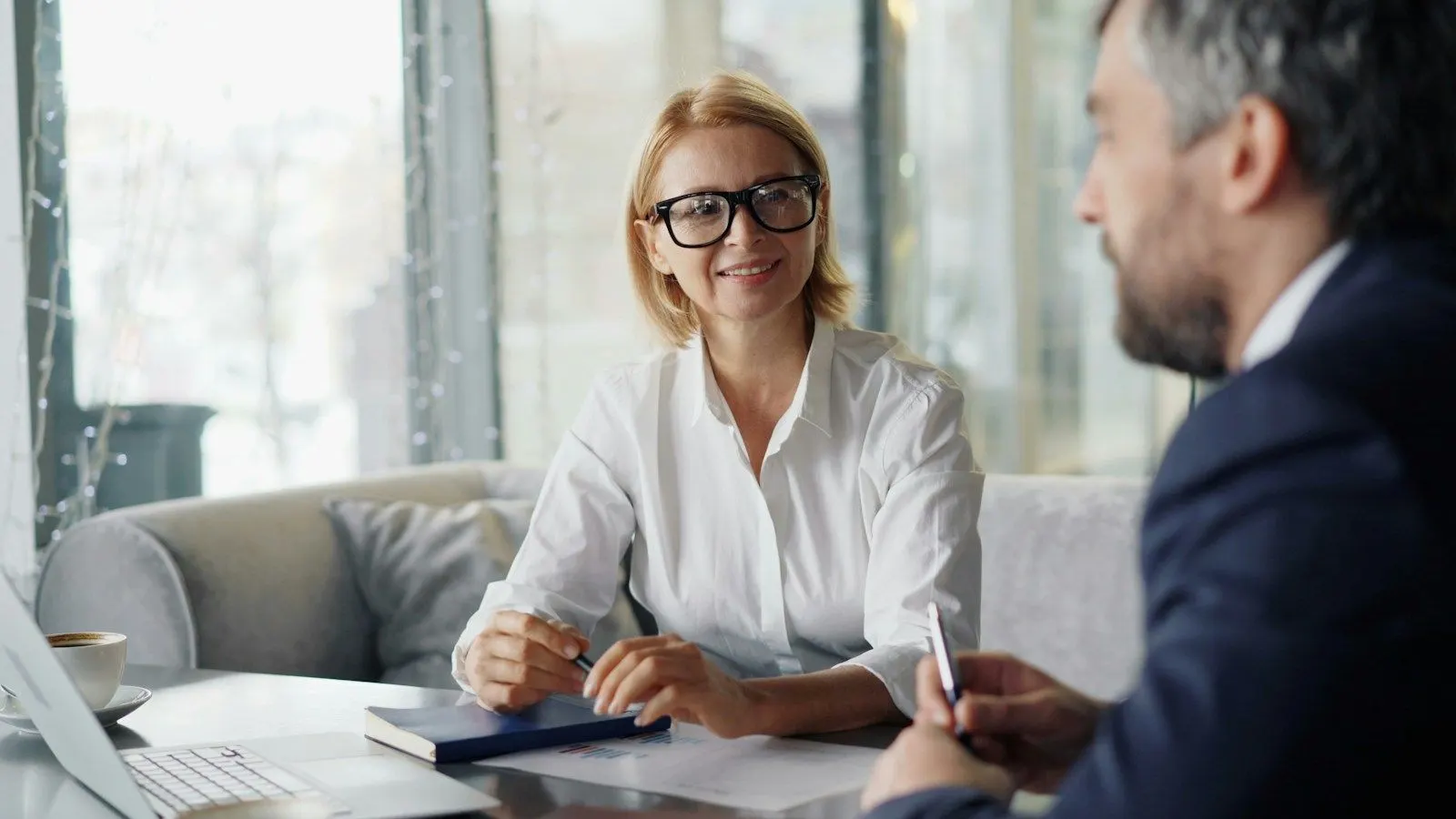 Two colleagues reviewing how to hire business analysts at a table beside a laptop.