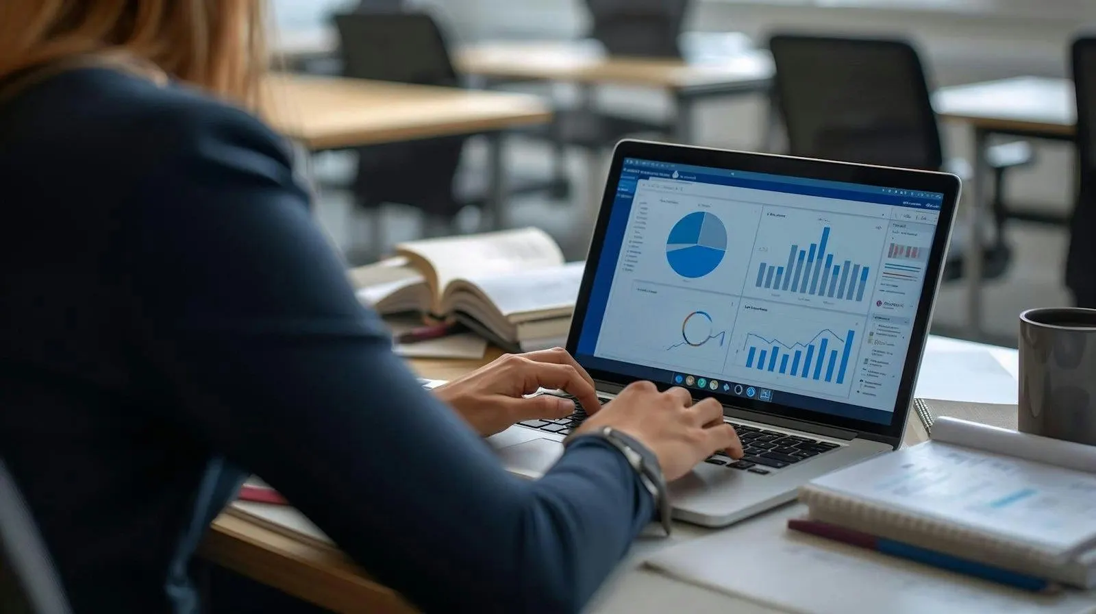A business analyst working through charts and graphs on a laptop at a desk.