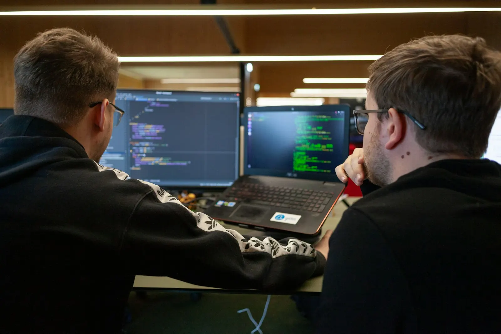 Two React developers pairing on code across a laptop and a pair of monitors.