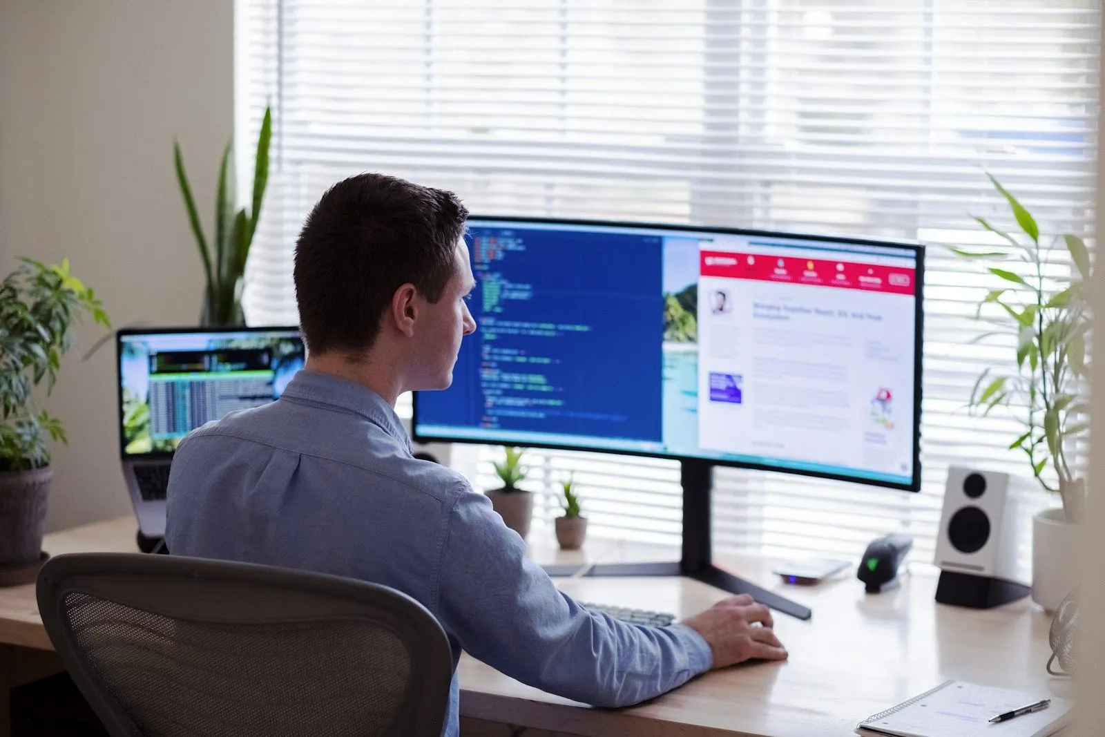 A React frontend architect writing code on a wide curved monitor beside a laptop.