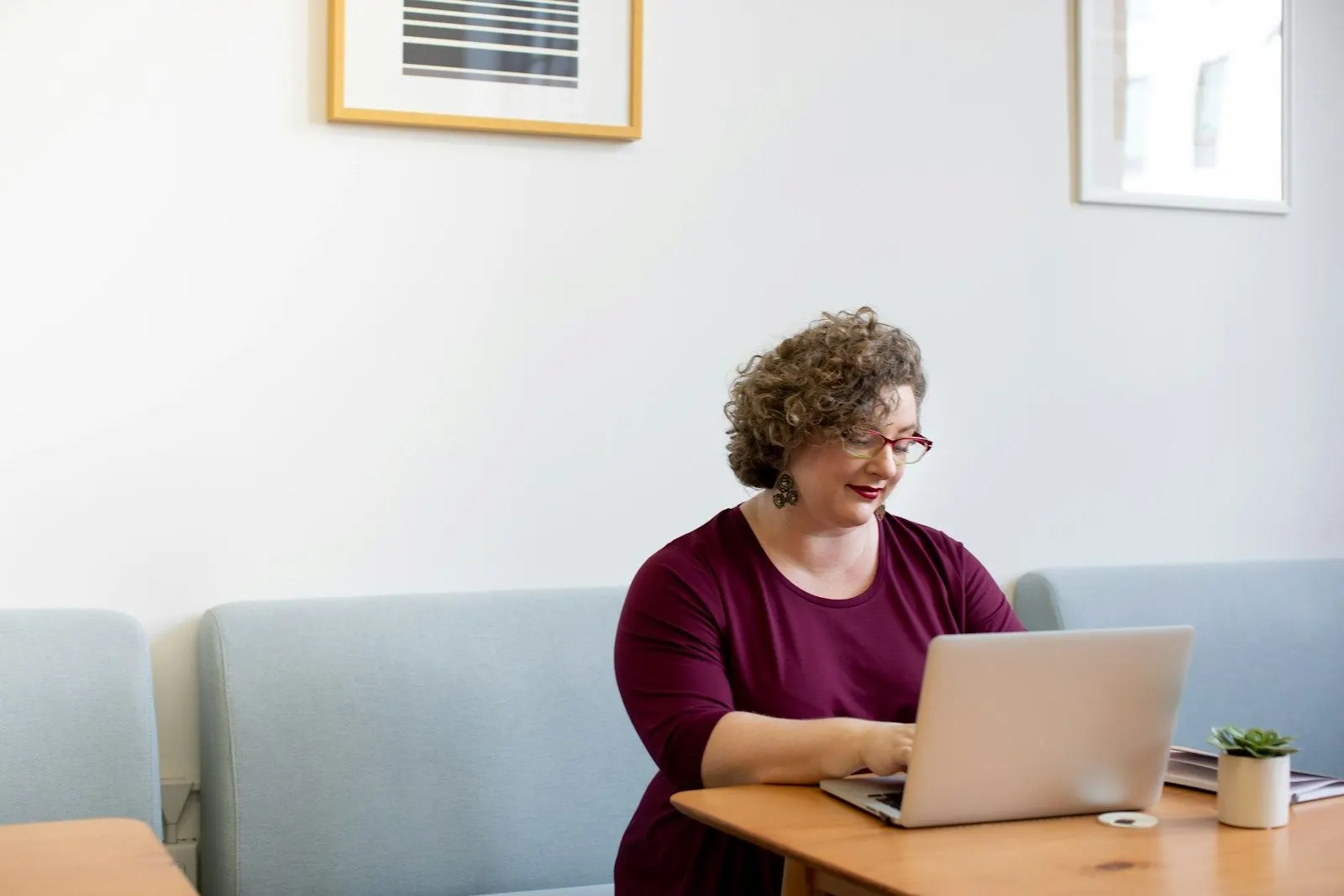 A React specialist working on a laptop at a table in a bright, airy room.