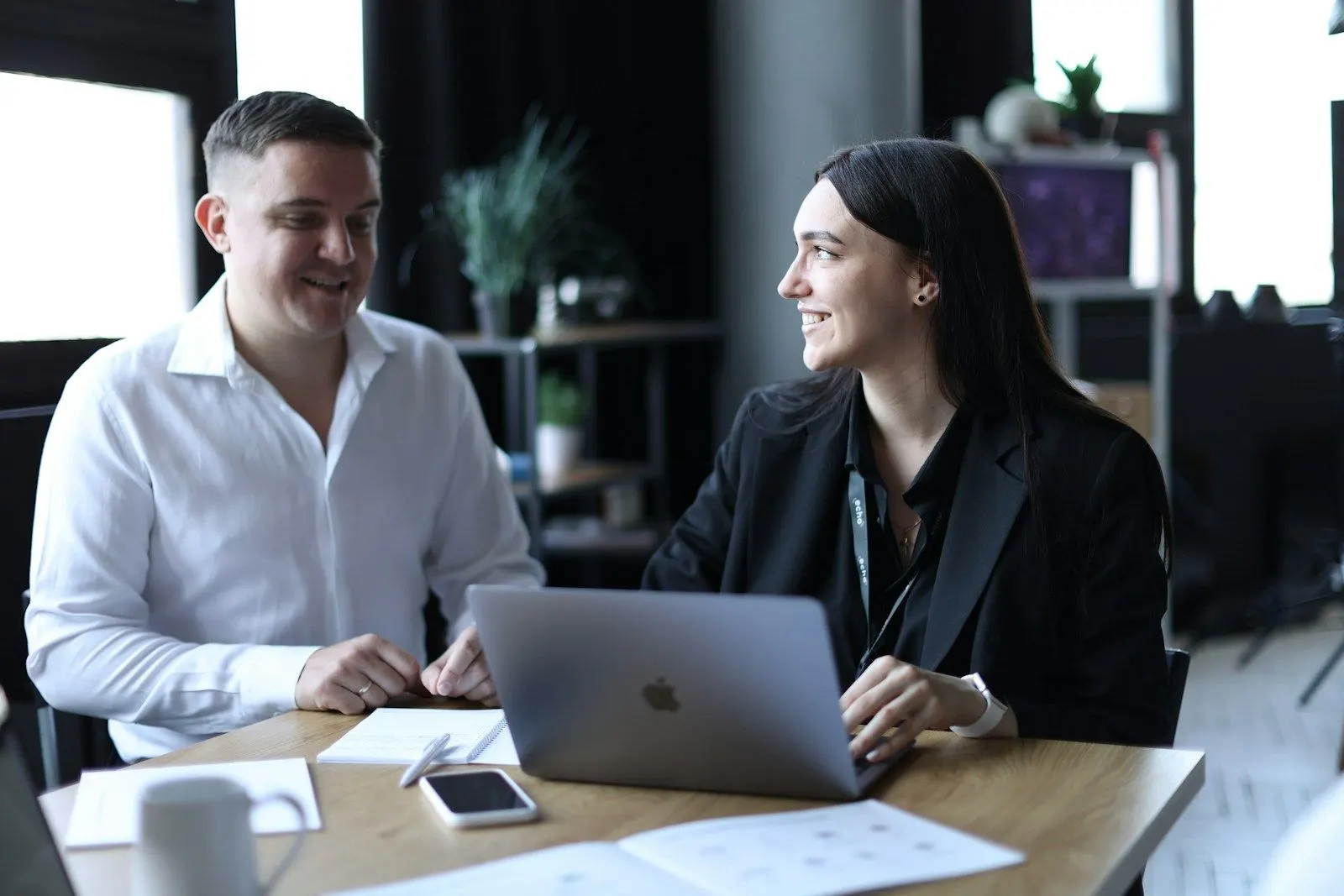 Two colleagues discussing how to hire a React developer over a laptop at a meeting table.