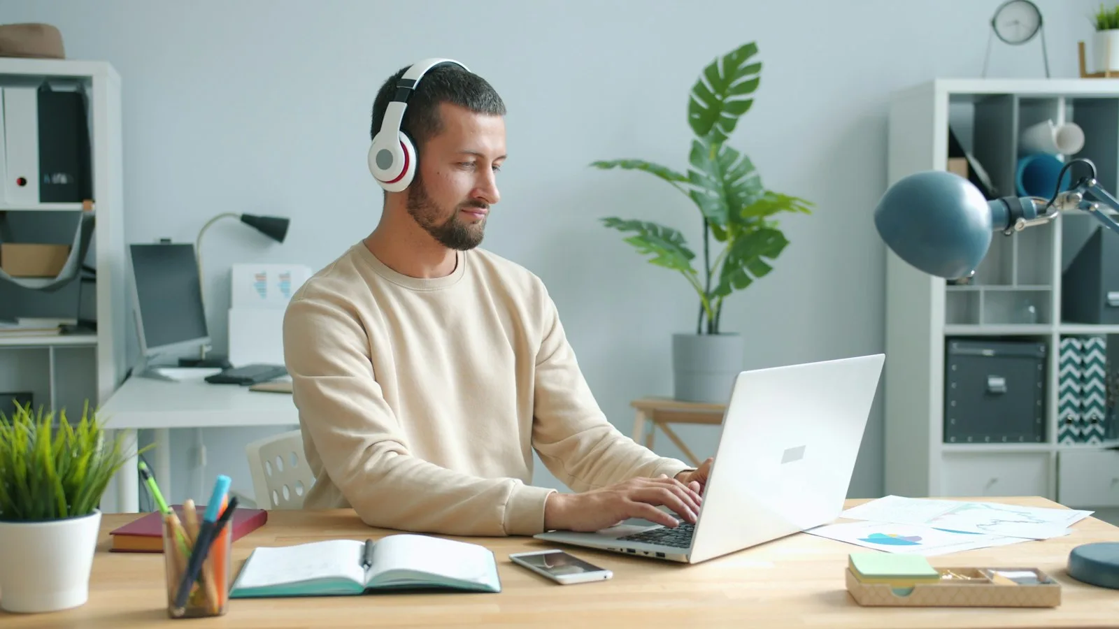 A fullstack developer with headphones working on a laptop at a bright desk.