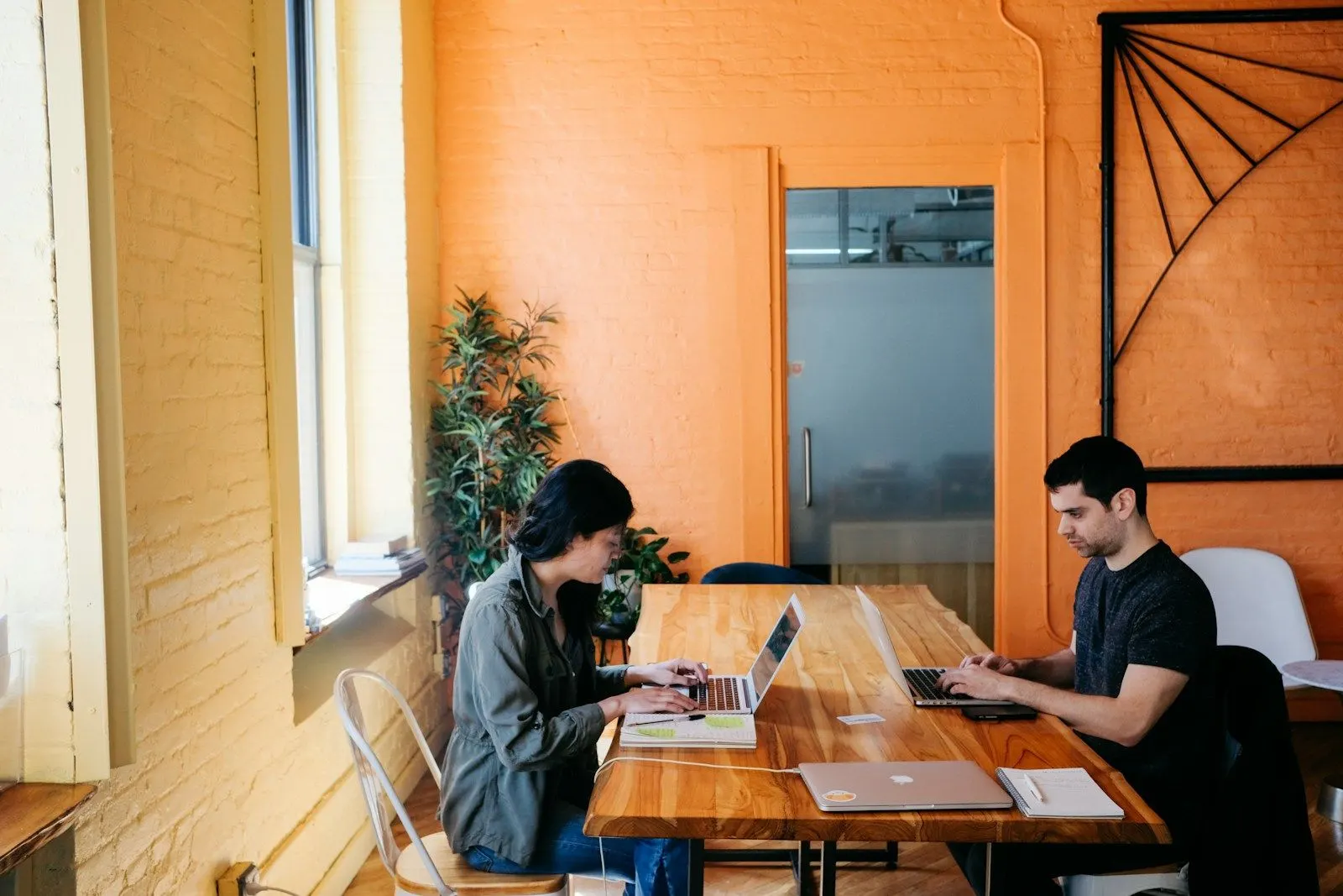 A fullstack tech lead working with a colleague on laptops at a long wooden table.