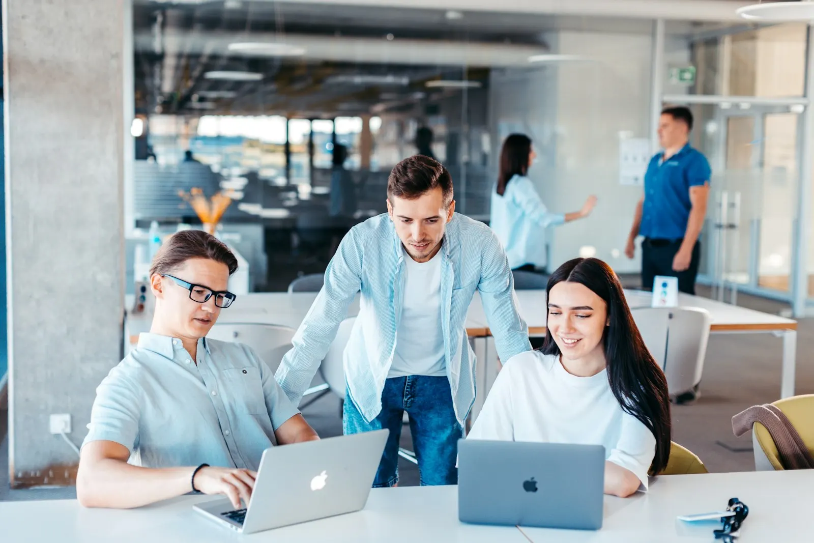 Three fullstack developers reviewing work together on two laptops in an open office.