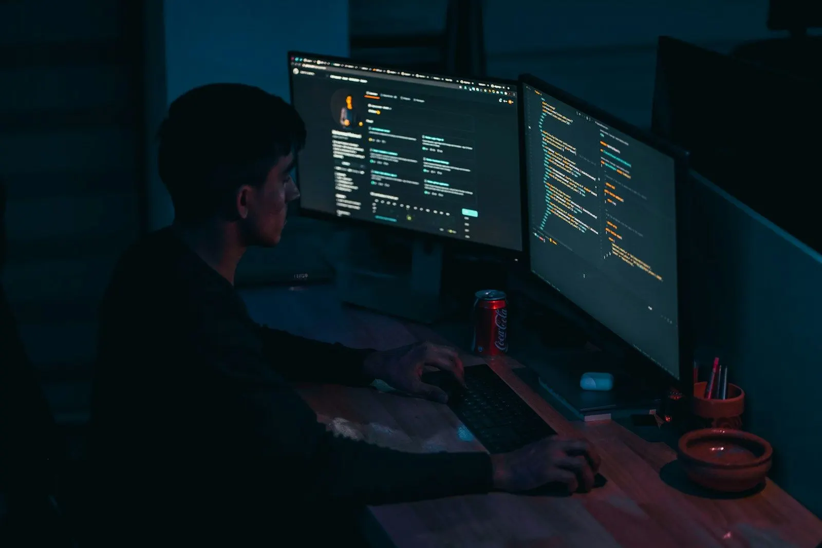 A Node.js backend architect working across two monitors full of code in a dim room.