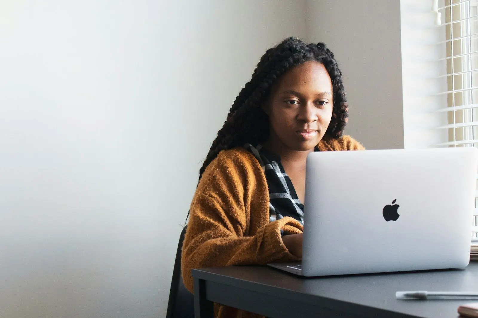 A Node.js specialist in a mustard cardigan working on a laptop at a desk.