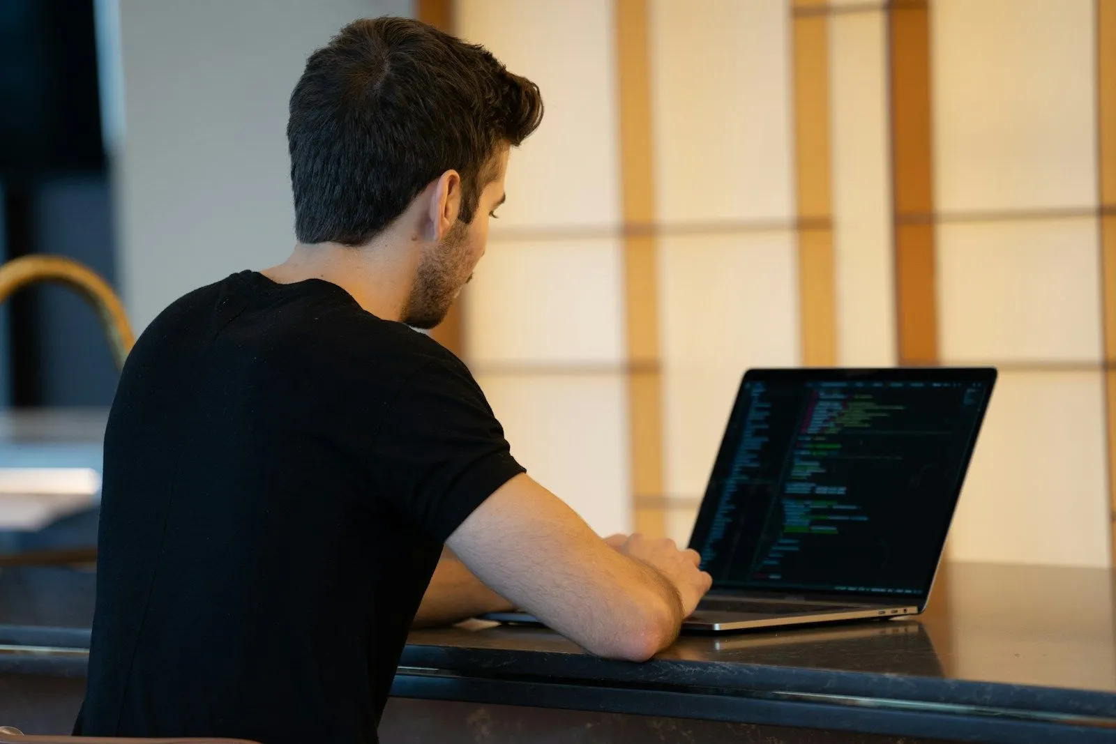 A Node.js developer in a black t-shirt writing code on a laptop at a desk.