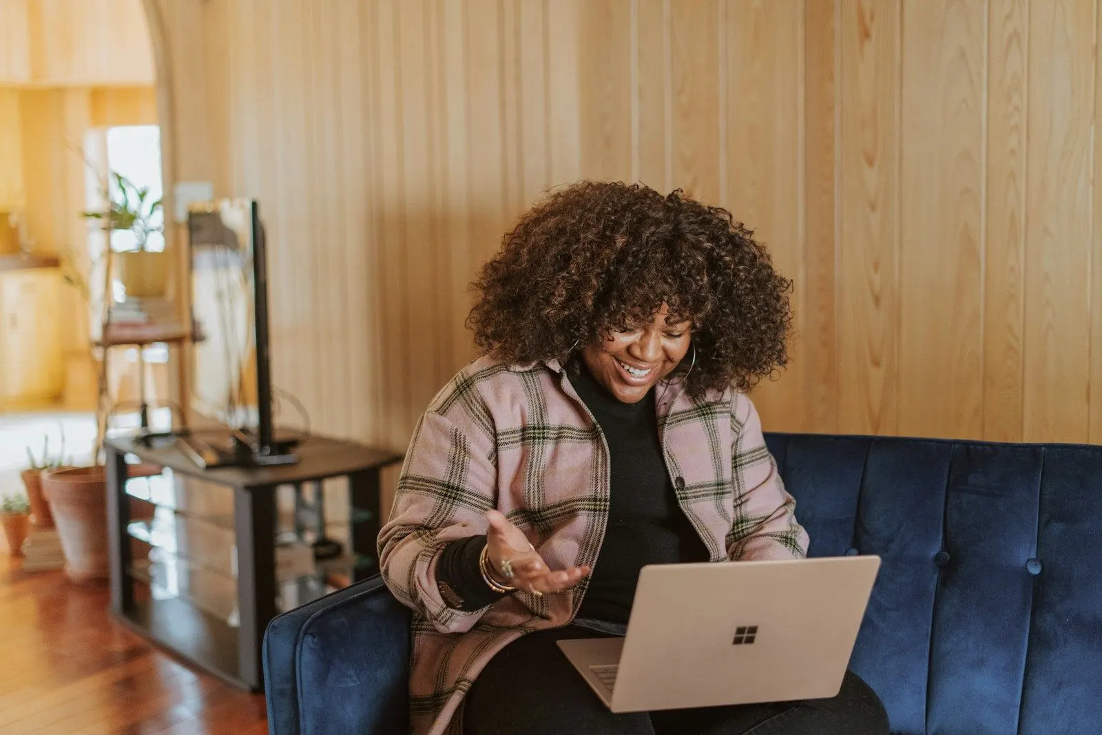 A Python specialist in a plaid shirt smiling while working on a laptop on a blue sofa.
