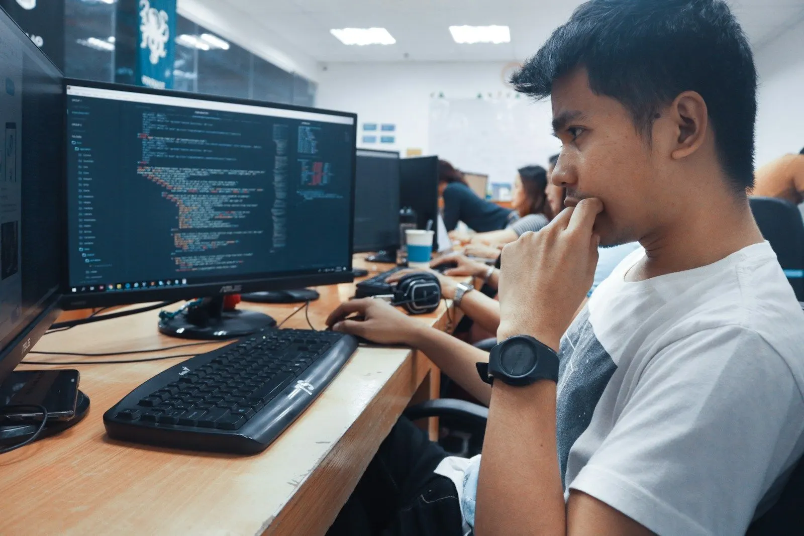 A Python data engineer thinking through code at his monitor in a busy office.
