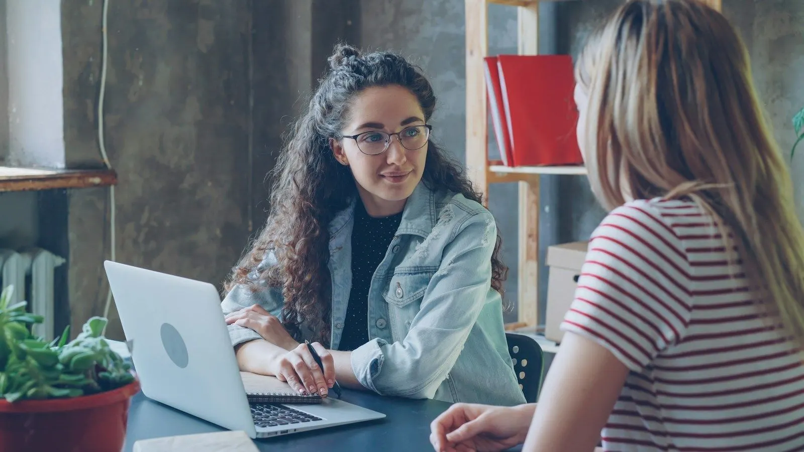 Two colleagues discussing how to hire a Python developer across a table beside an open laptop.