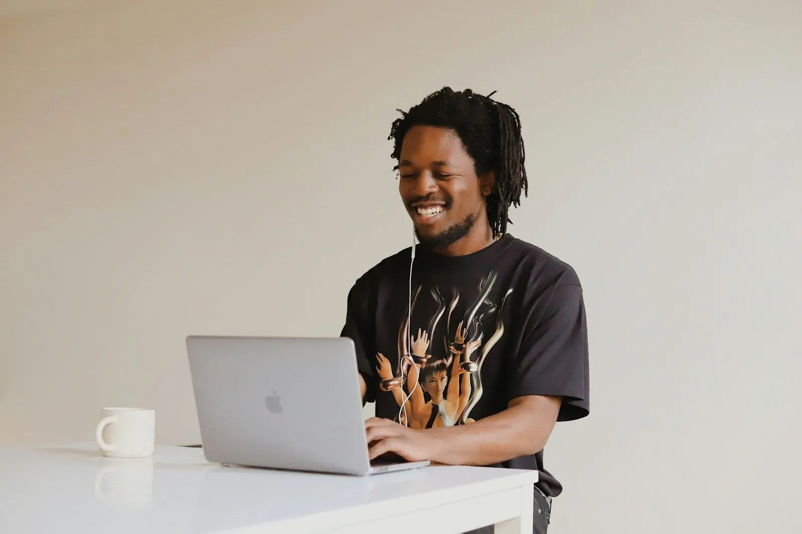 A Python developer in a black t-shirt smiling as he works on a laptop at a white desk.