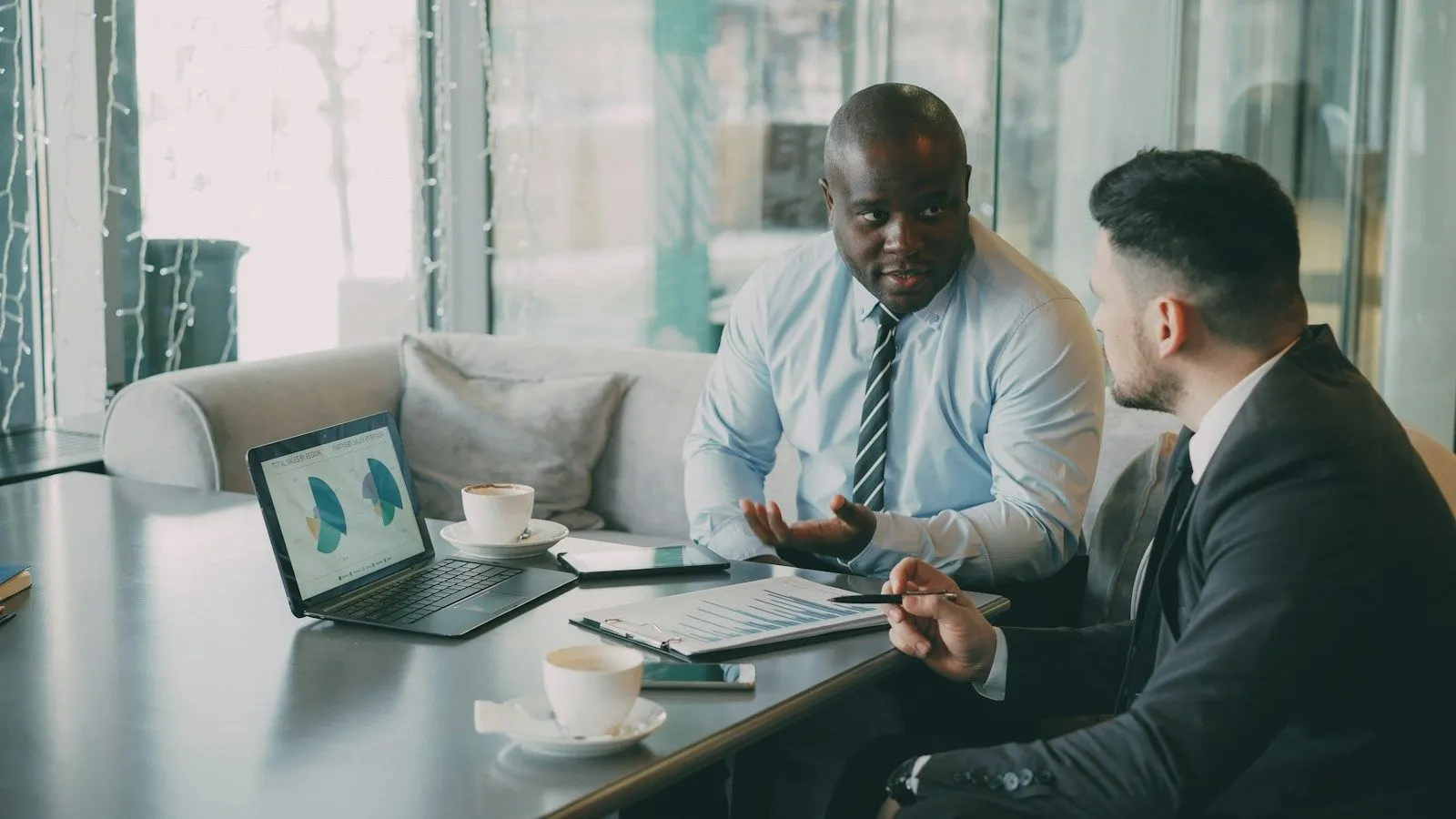 Two colleagues discussing how to hire a .NET developer on a laptop in a glass-walled lounge.