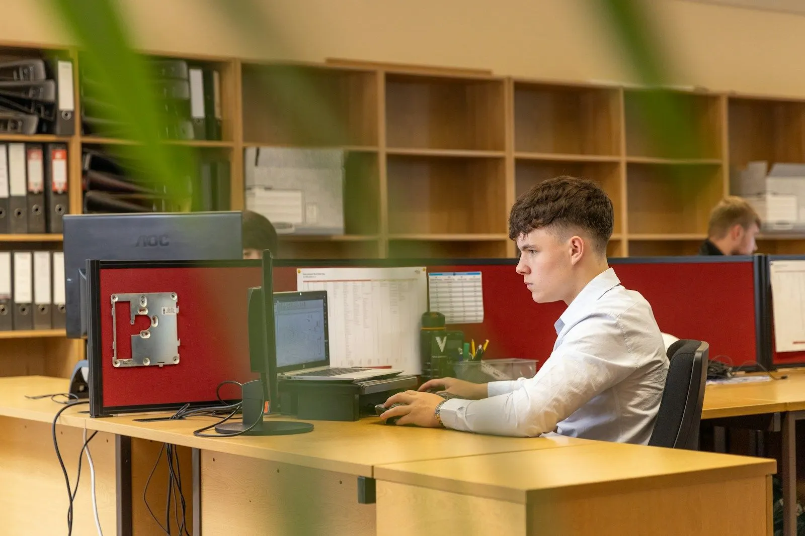 A young .NET developer working at a desk with two monitors in an office.