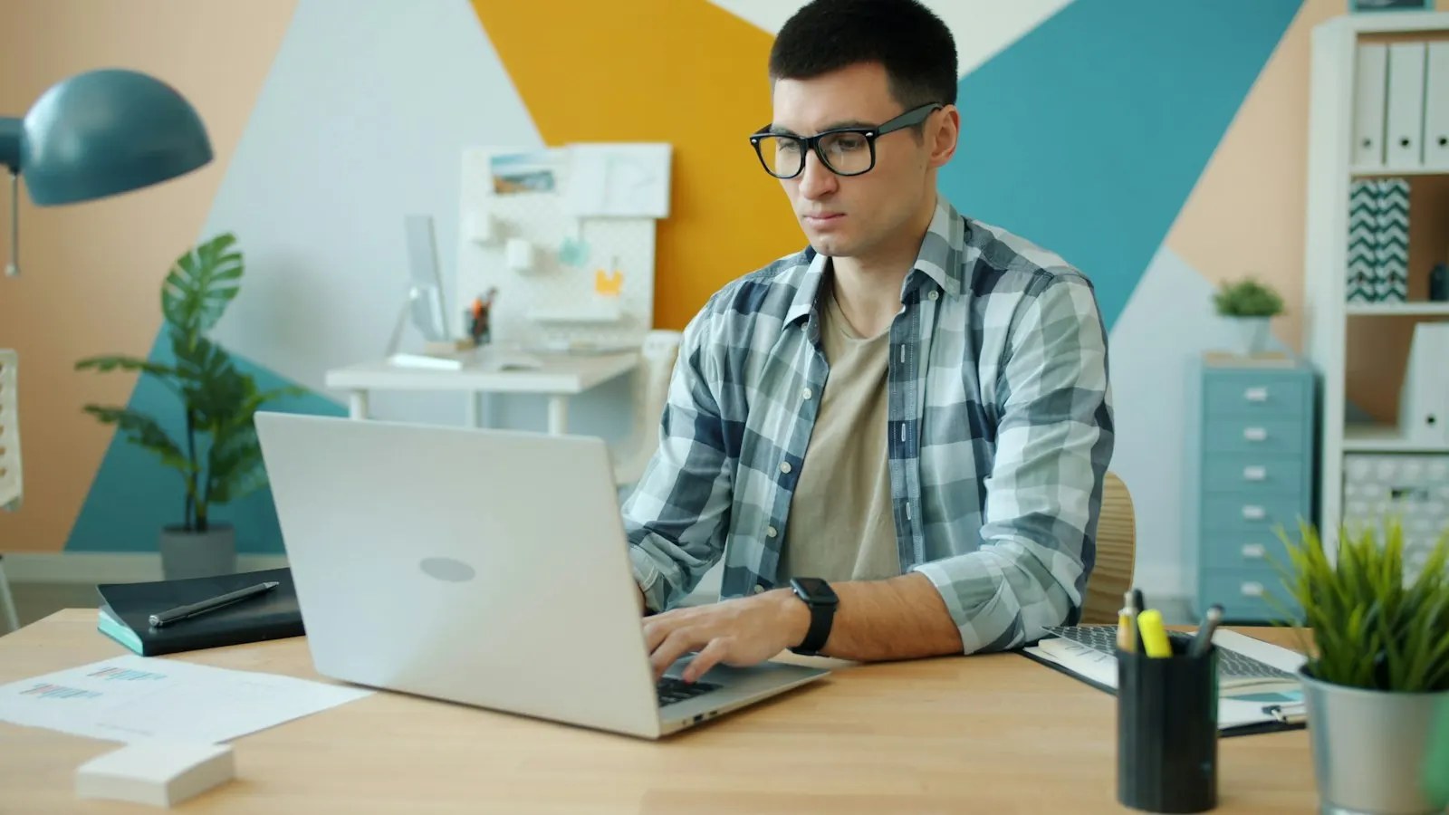 A Java developer in glasses typing on a laptop at his desk.