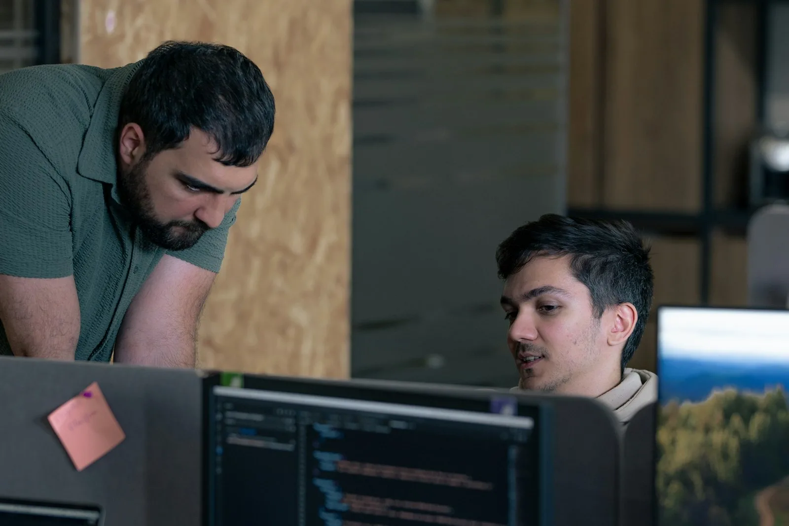 Two Java developers reviewing code together at a desk with monitors.