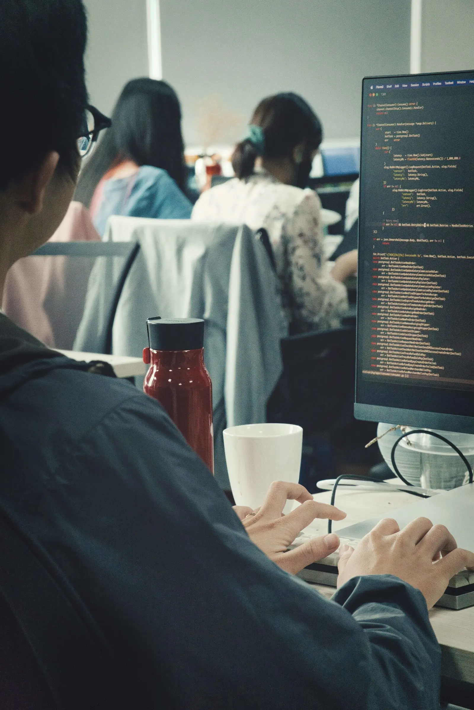 A Java engineer writing code at a monitor in a busy office.