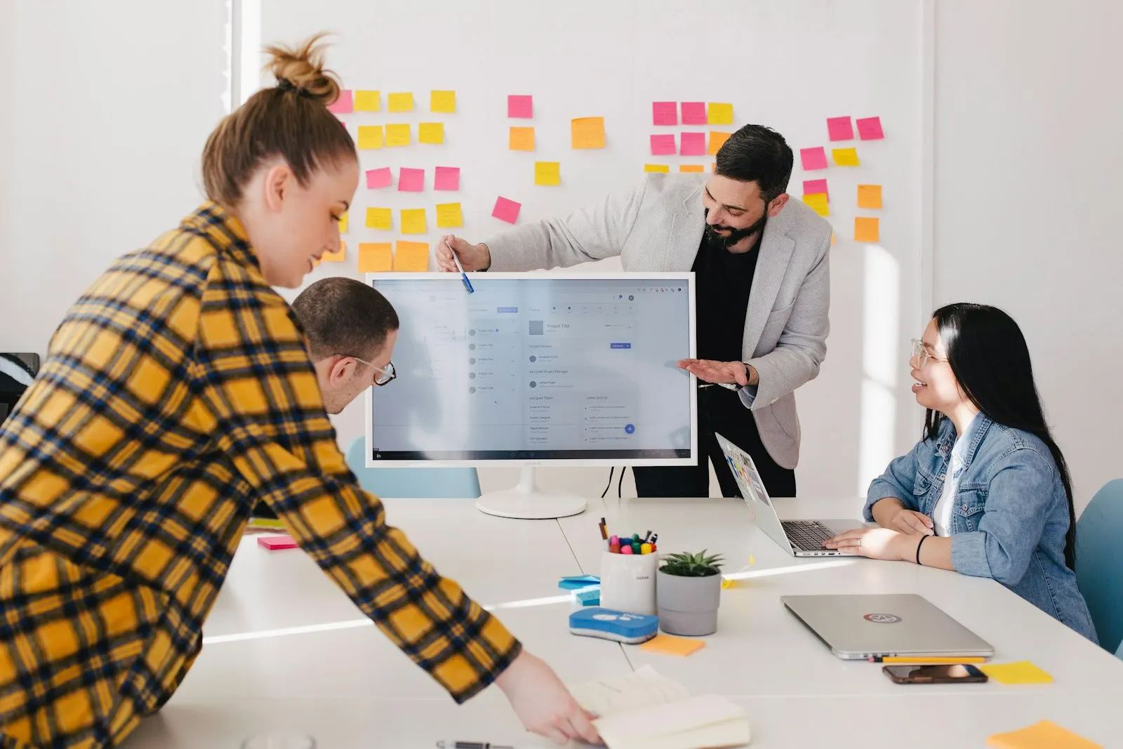 A product discovery team reviews a design on screen, with sticky notes on the wall behind them.