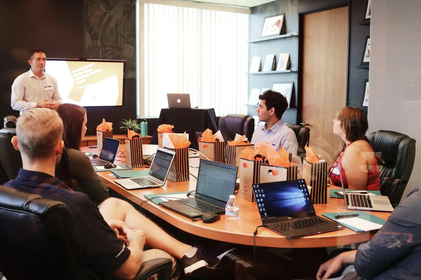 A PHP team listening to a colleague present in a meeting room, laptops open.