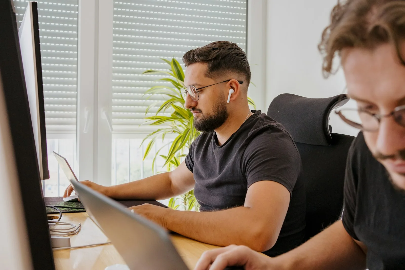 A PHP developer working at his laptop beside a colleague in a bright office.