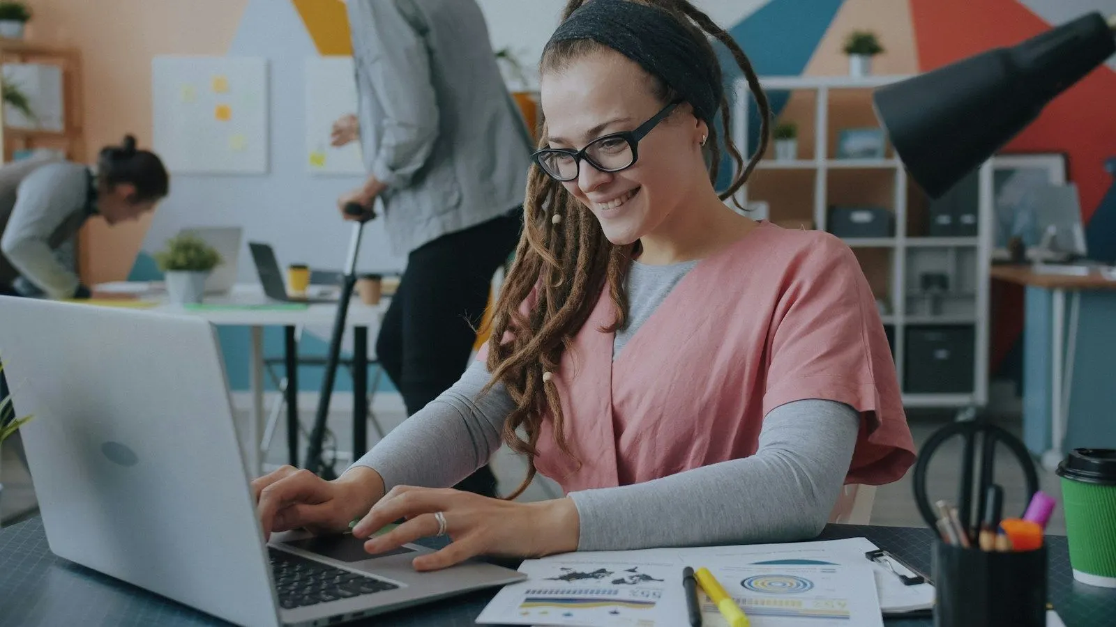 A Laravel specialist smiling while working on her laptop in a colourful office.