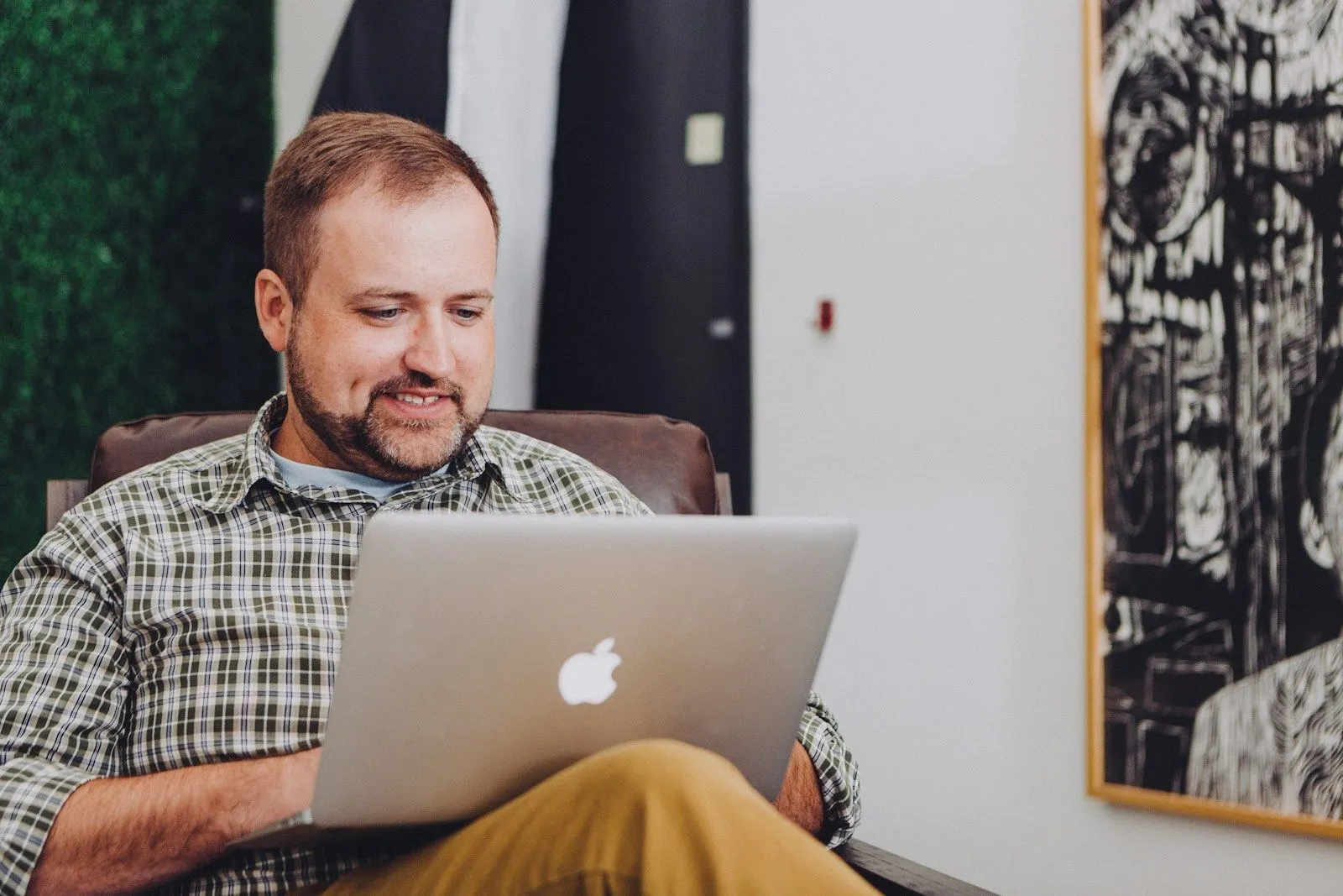 A PHP modernisation engineer in a plaid shirt working on a laptop in his lap.