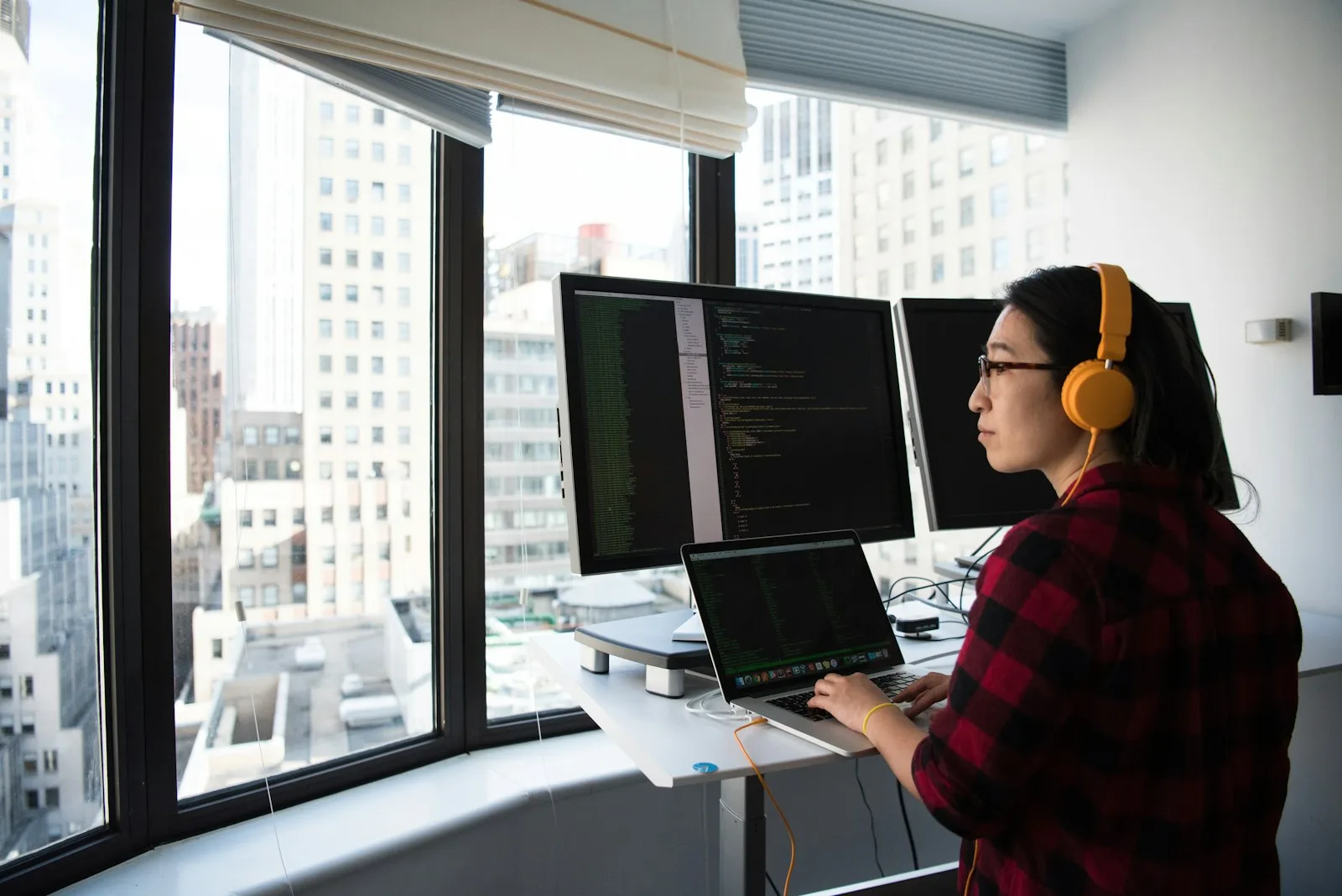 A Kotlin developer in headphones writing code at a standing desk with two monitors and a laptop.