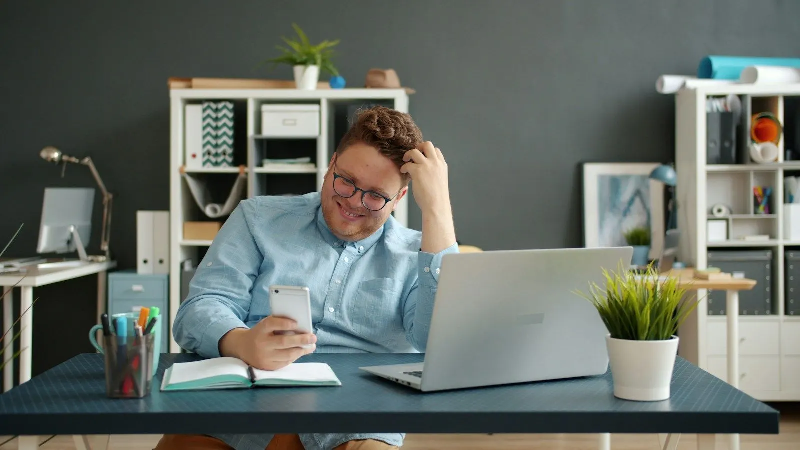 A Kotlin architect in glasses checking an app on his phone beside his laptop.