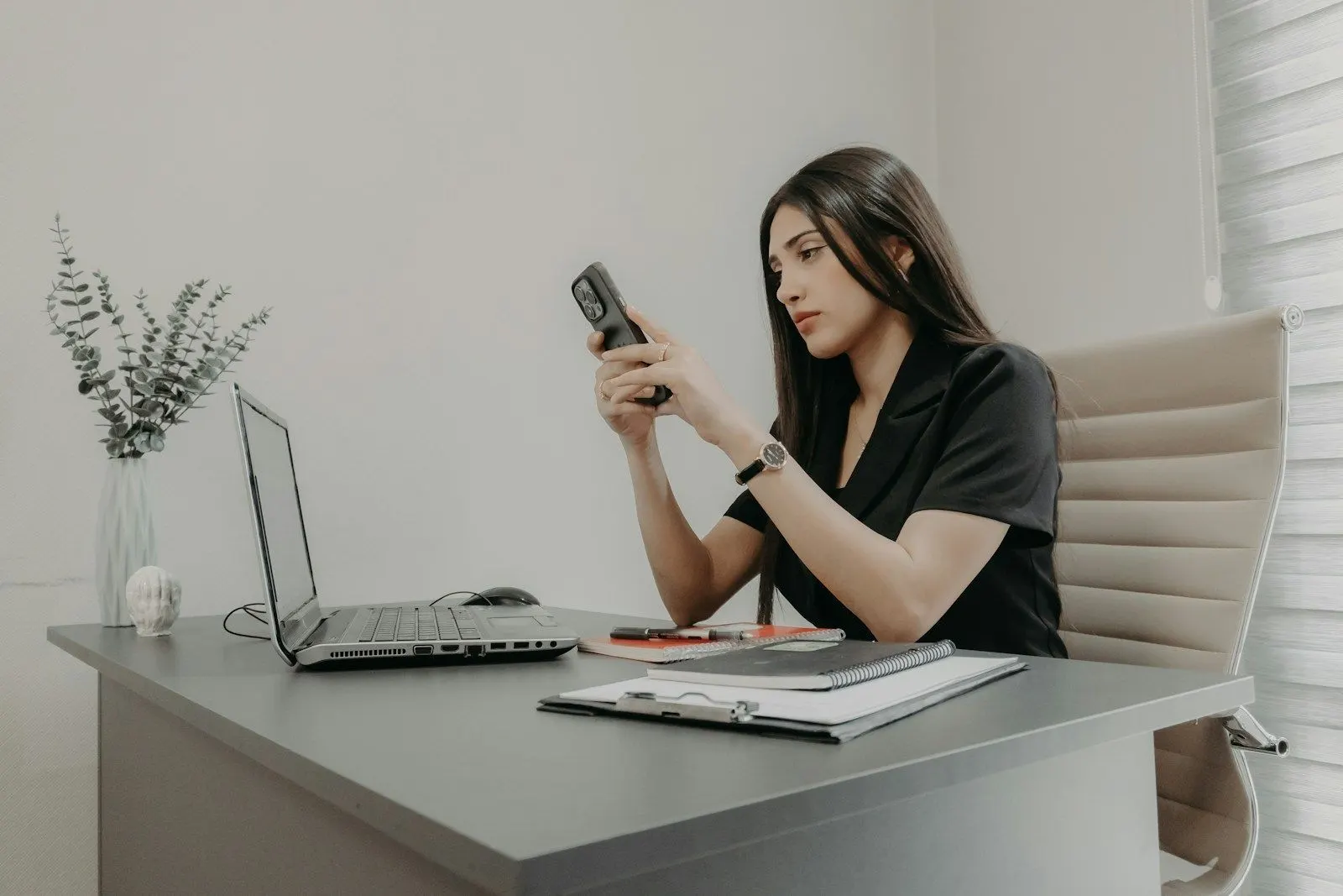 A senior Android engineer in Kotlin checking her phone at her laptop desk.