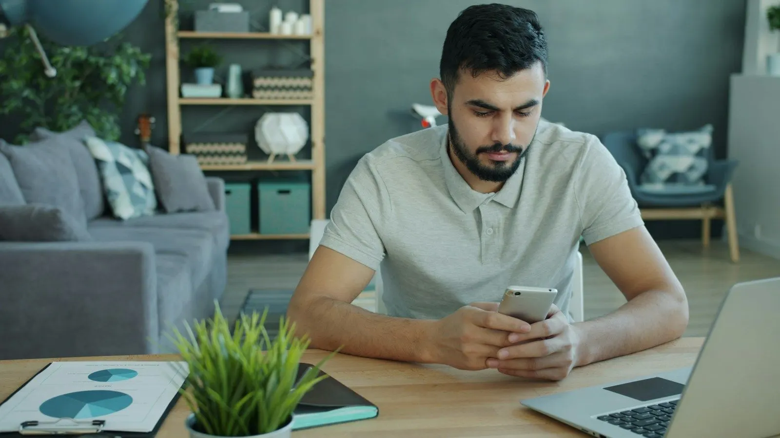 A Kotlin Multiplatform engineer checking his smartphone beside a laptop at his desk.