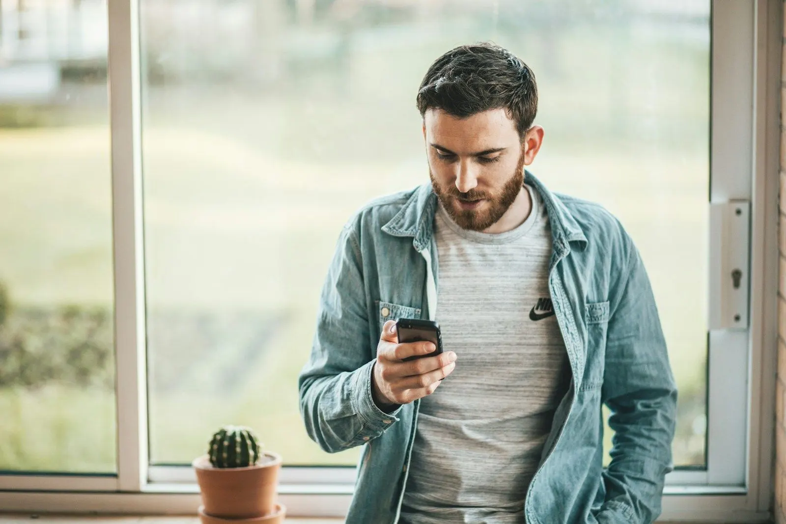 A Kotlin backend engineer checking his phone by a bright window.