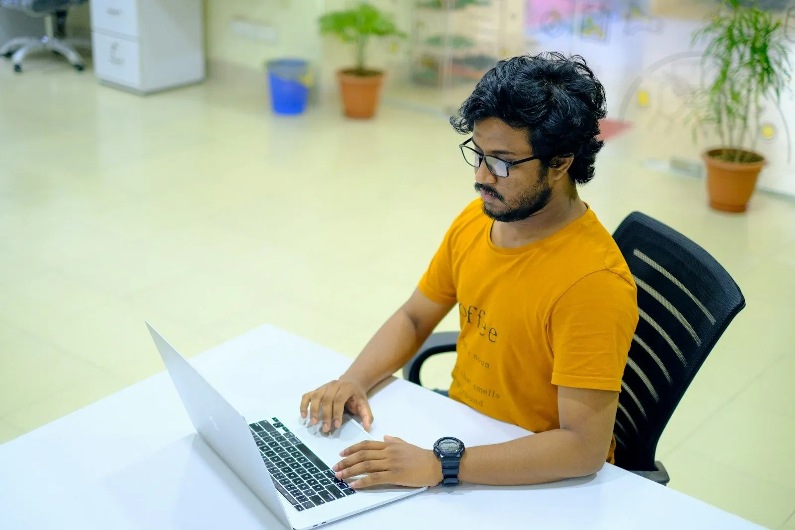 A Kotlin developer in an orange t-shirt working on a laptop at a white desk.