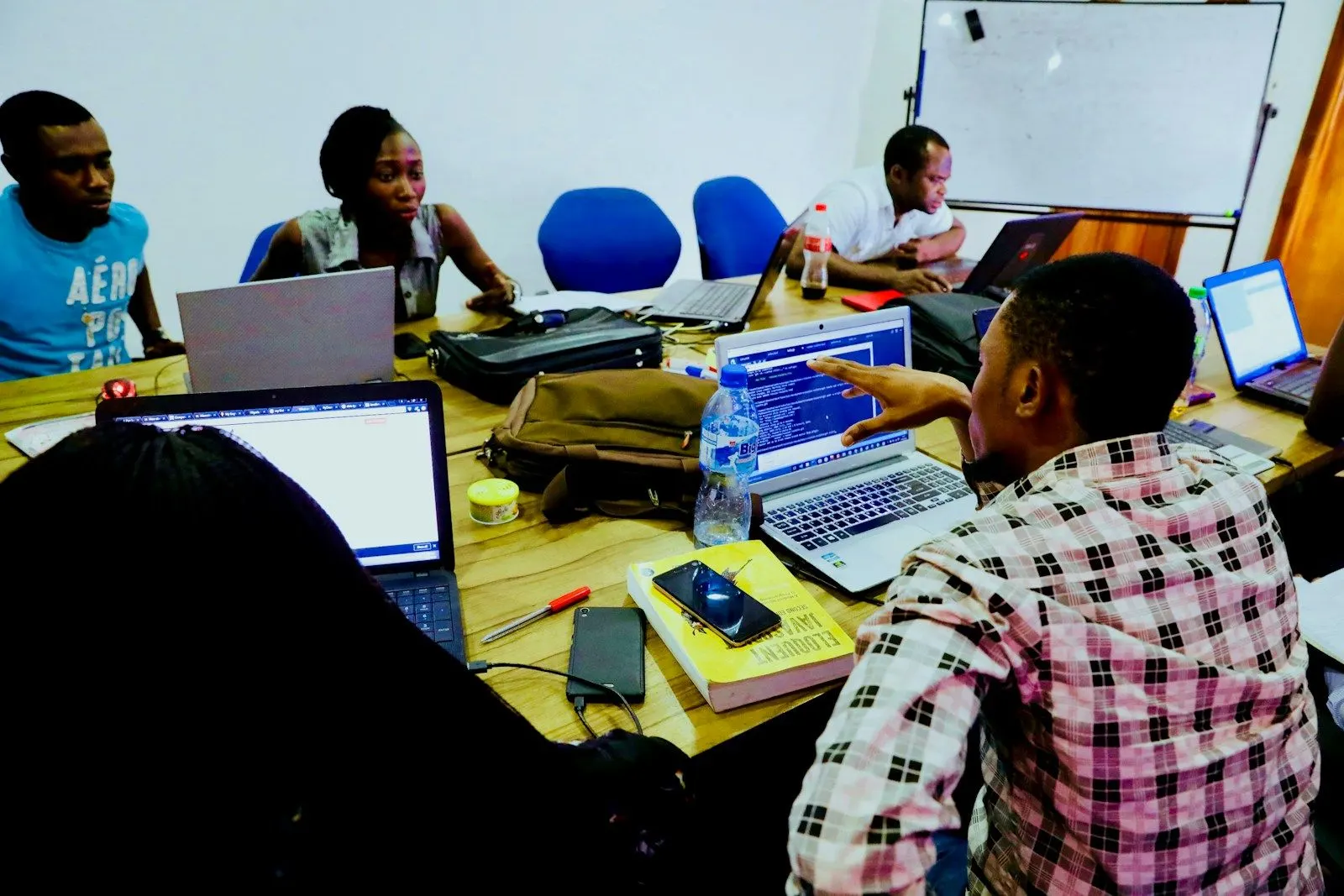 A group of React Native developers working on laptops around a shared table, one pointing at a screen.