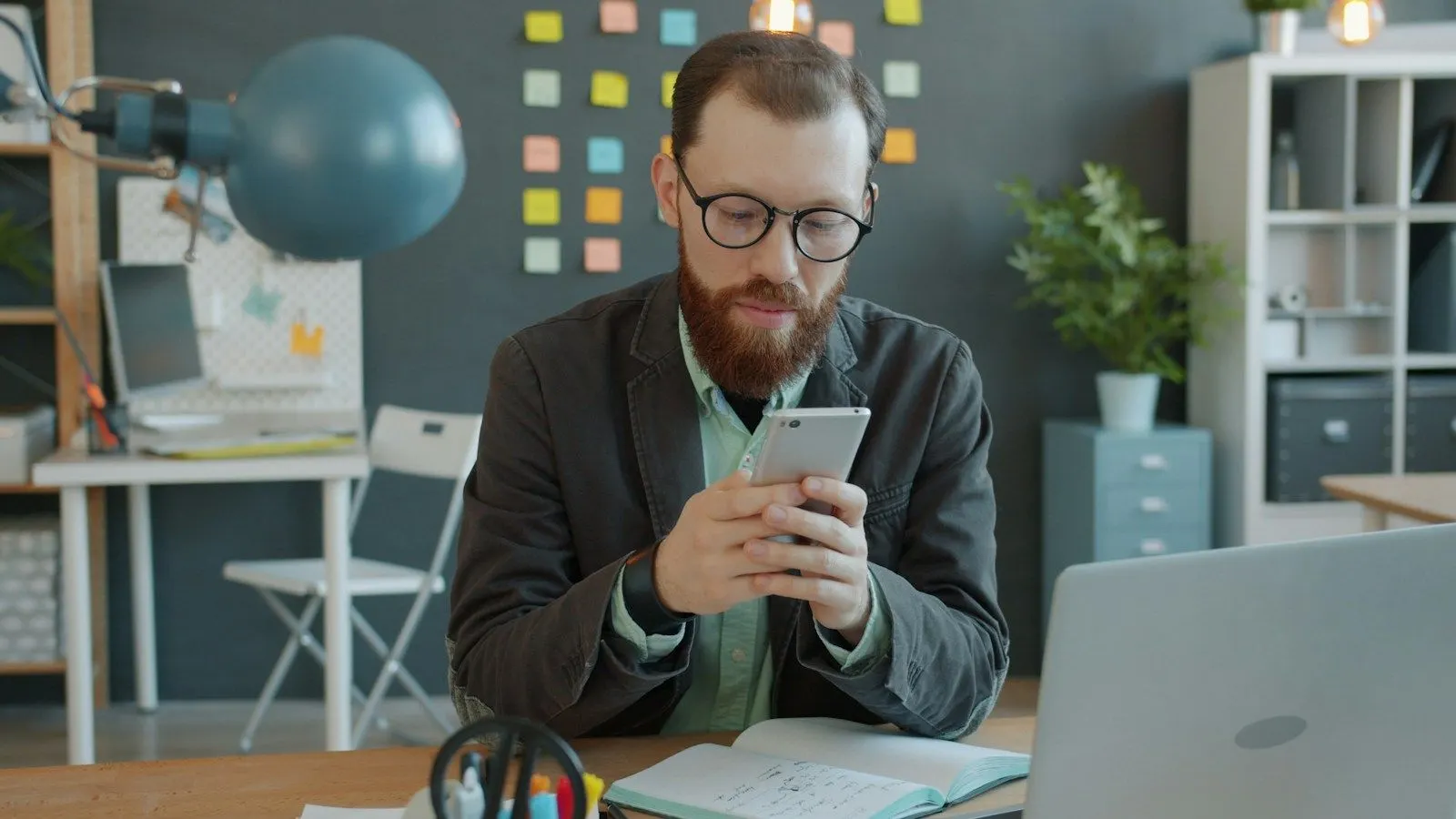 A React Native specialist in glasses checking an app on his phone at his laptop.