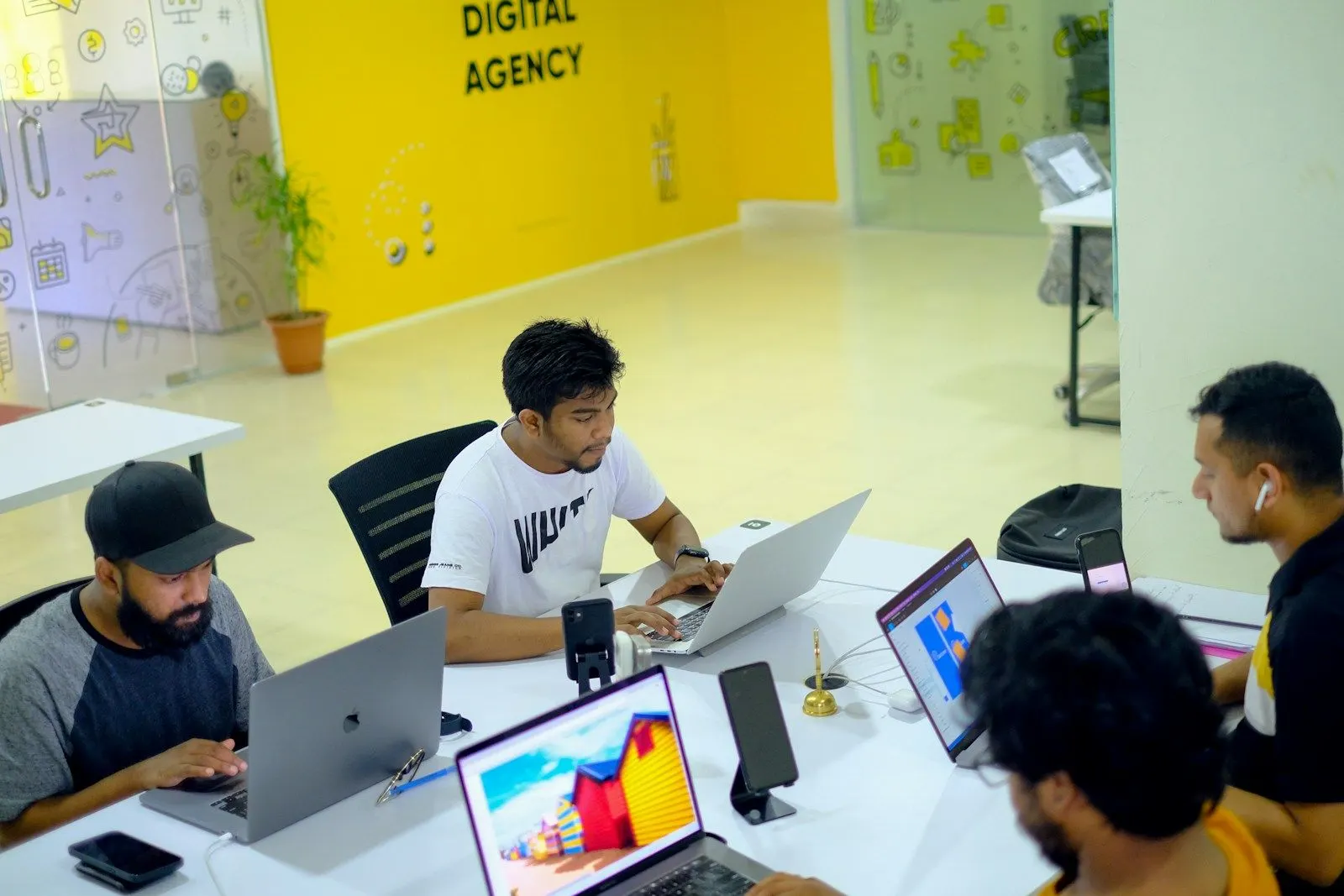 A Flutter team working on laptops around a table in a bright yellow studio.