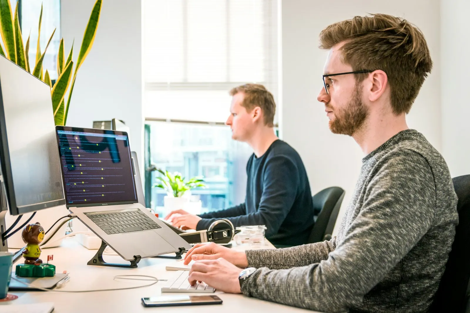 Two Flutter developers working side by side at their desks in a bright office.