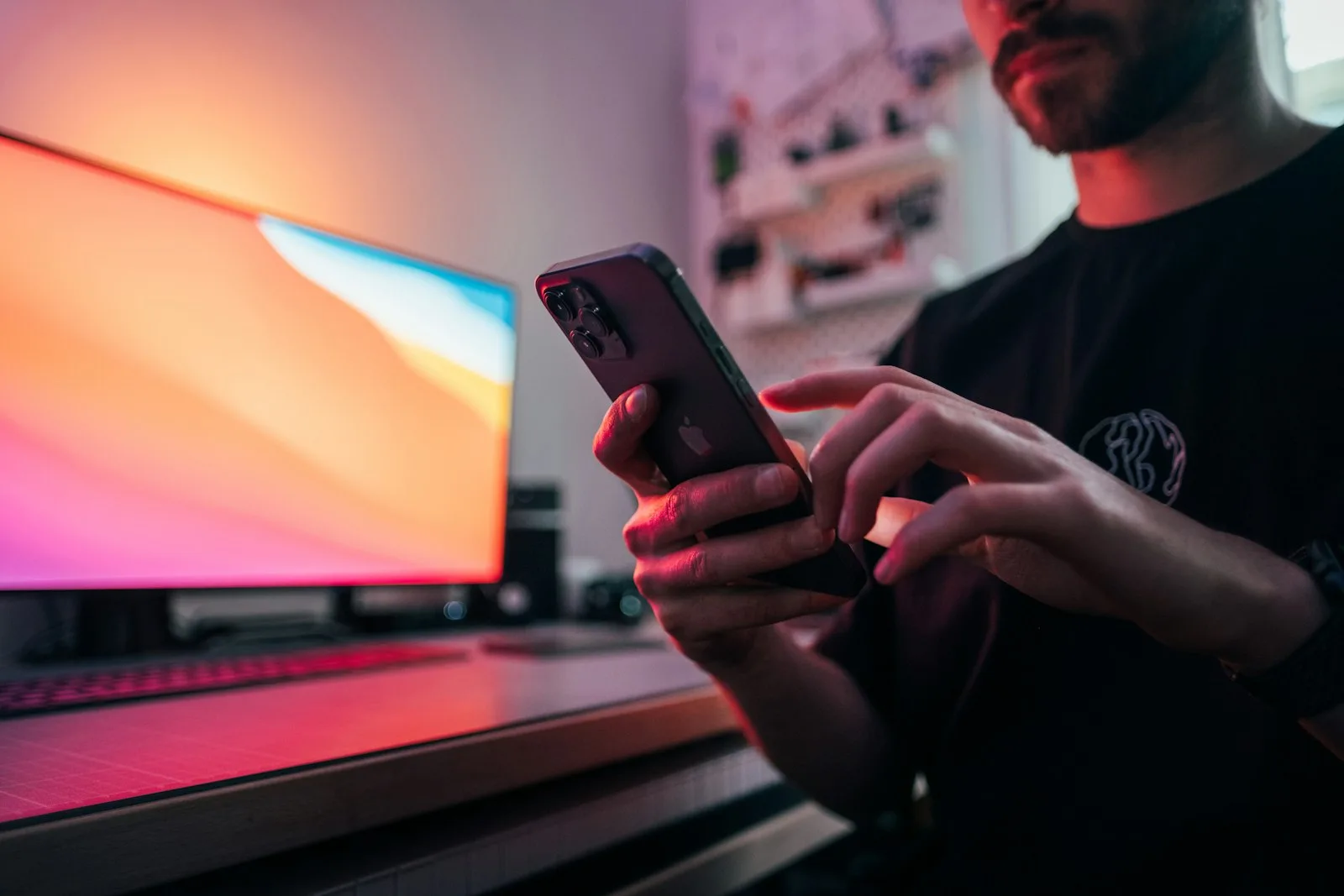 A Flutter developer checking an app on his phone beside a glowing monitor.