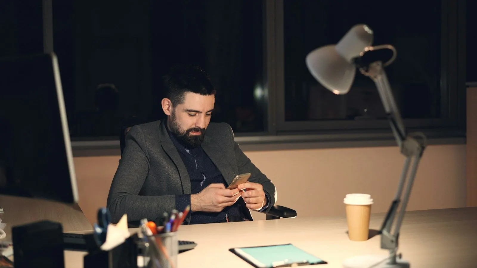 A Flutter release engineer in a blazer checking his phone at his desk in the evening.