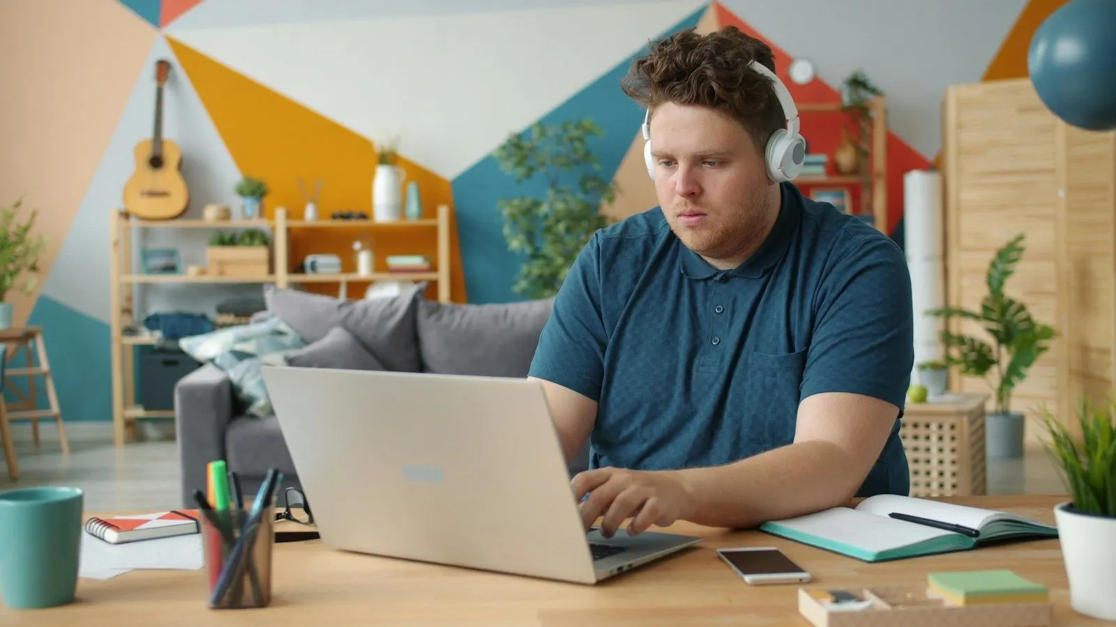 A Flutter developer wearing headphones working on a laptop at a bright home desk.